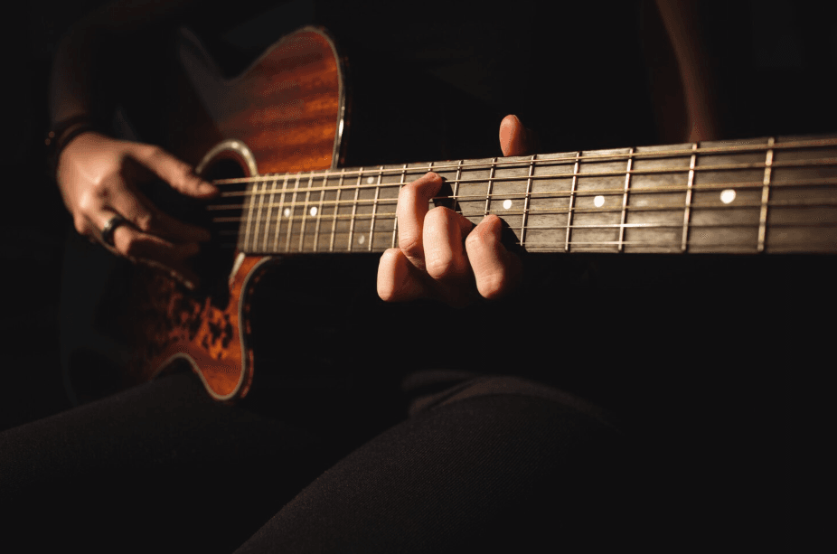 Manos tocando una guitarra acústica con luz cálida sobre fondo oscuro
