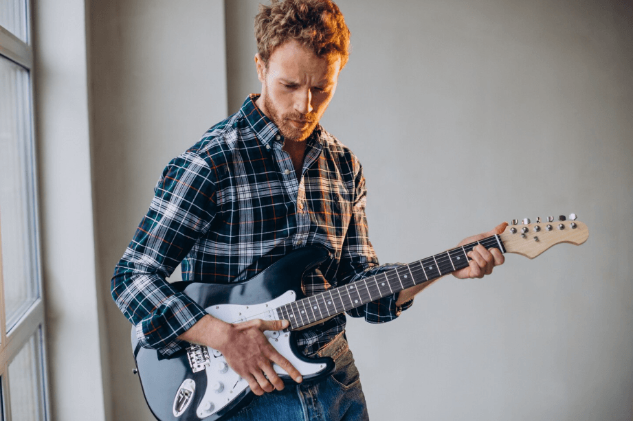 Guitarrista concentrado tocando una guitarra eléctrica negra junto a una ventana